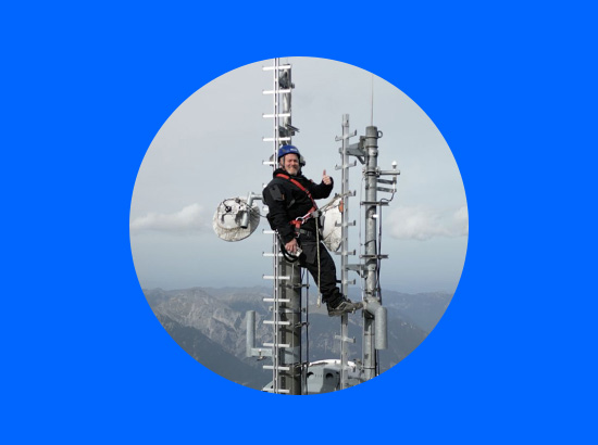 Netztechniker auf einem Mobilfunkmast vor einem Bergpanorama